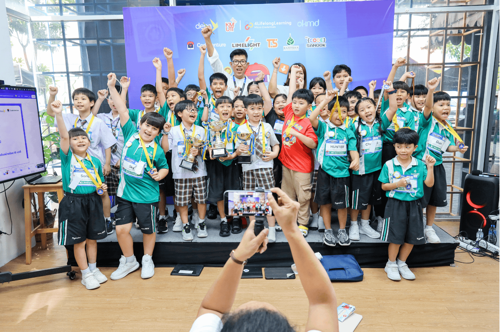 เยาวชนชูมือฉลองบนเวทีพร้อมถ้วยรางวัล